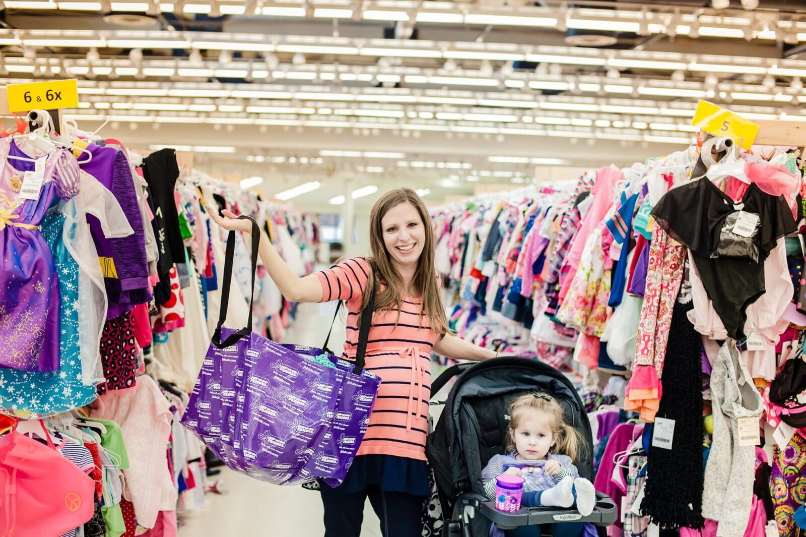 Two masked moms—one holding a child with a mask, the other pregnant—shop for their families at the local JBF sale.